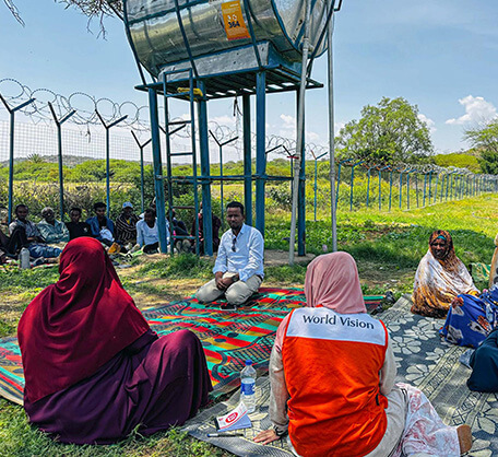 水タンクの下で支援スタッフと村人が意見交換。地域開発プログラムにより持続可能な生活基盤づくりを目指す。