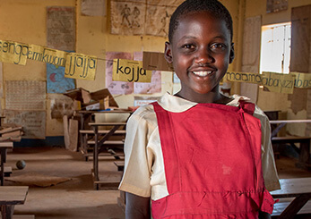 教室で笑顔を見せるアフリカの少女。教育支援により学ぶ機会を得た子どもたちの明るい未来を象徴する場面。