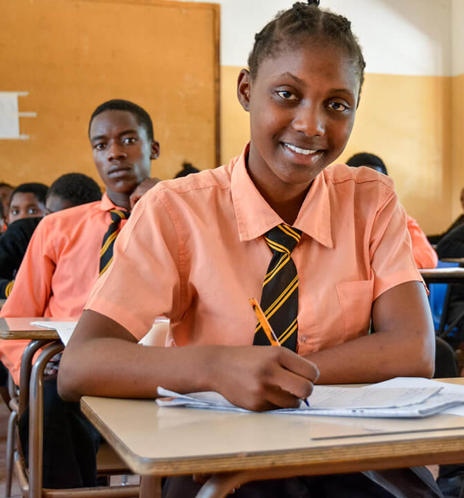 教室で笑顔を見せながらノートを取る女子生徒。教育支援が子どもたちの未来を広げる様子を示す情景。