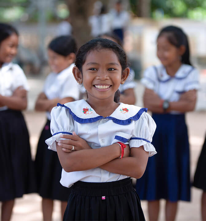 制服姿で腕を組み、誇らしげに立つ女子児童。教育支援が子どもたちの未来を明るくすることを示す情景。