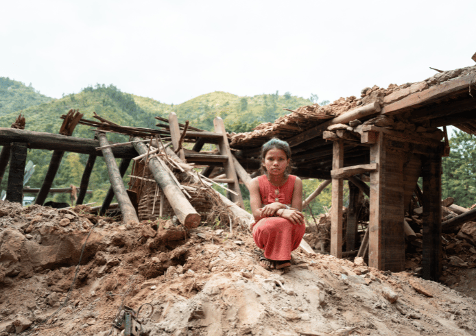 倒壊した建物の前にたたずむ少女。衛生環境の悪化や感染症リスクに対応する健康支援の必要性を訴える。