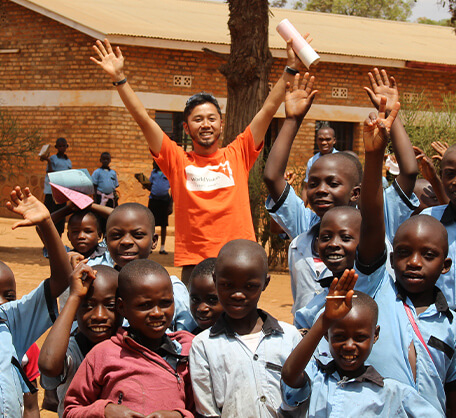 笑顔で手を挙げるアフリカの子どもたちと支援スタッフ。教育支援と子どもの権利保護を推進するアドボカシー活動の一場面。