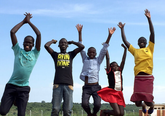 屋外で並んでジャンプする子どもたち。アドボカシー活動を通じた子ども支援と未来への希望を表現する瞬間。