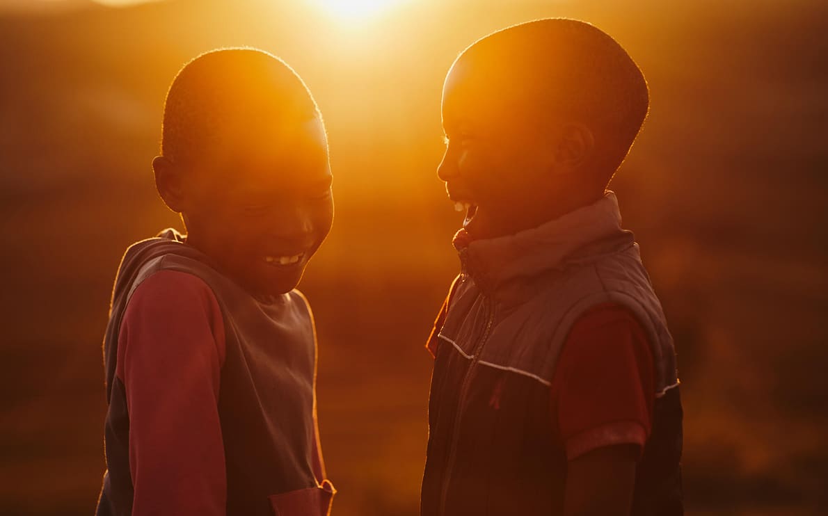 夕陽に照らされ、笑顔で向き合うアフリカの子どもたちが友情と喜びを分かち合う瞬間。