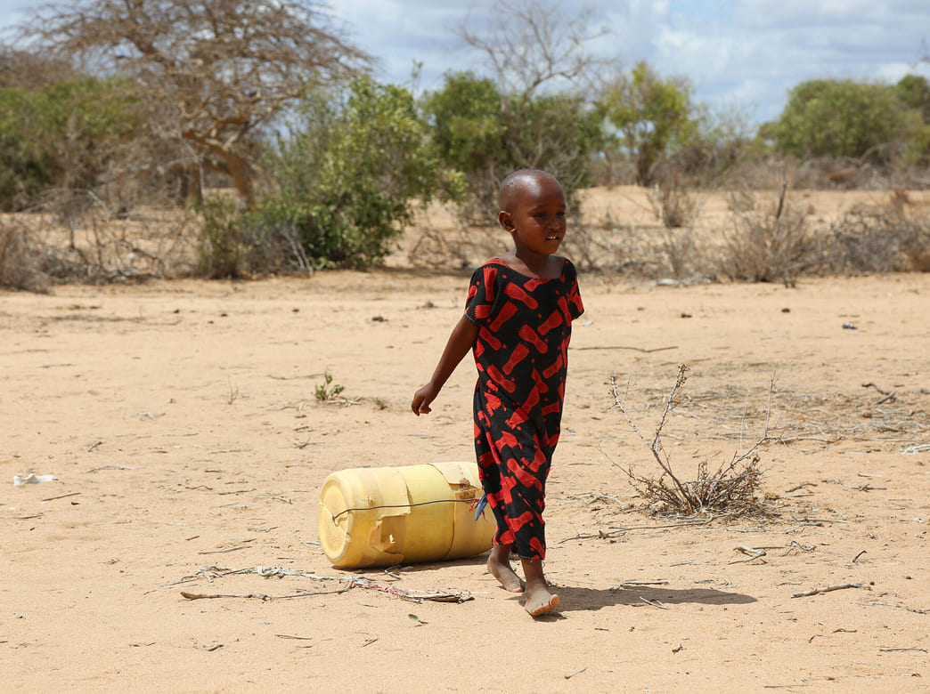 水汲みのため、裸足で黄色いタンクを転がしながら歩く小さな子ども。