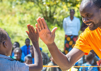 ワールド・ビジョンのスタッフと子どもが笑顔でハイタッチし、信頼と喜びを分かち合う瞬間。
