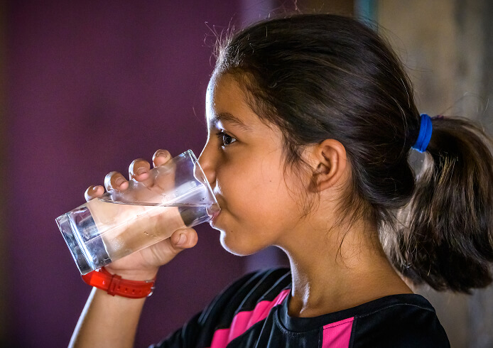 清潔な水をコップで飲む少女。安全な飲料水の提供が子どもたちの健康と生活を守る取り組みの一環。