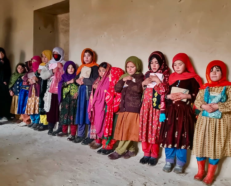 色とりどりの民族衣装を身にまとった女の子たちが教室で学びに向き合う姿。教育支援による変化を象徴。