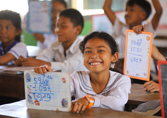 支援を受ける子どもたちが教室で笑顔を見せ、学習成果を見せ合う様子。