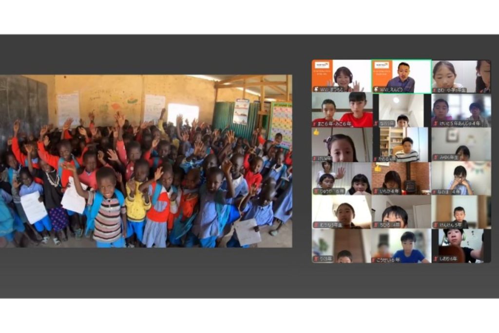 Group of smiling children in a classroom raising hands, alongside a grid of online students in a video conference.