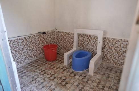 Small children’s potty chair with a blue basin on a white stand in a tiled bathroom, with a red bucket nearby.