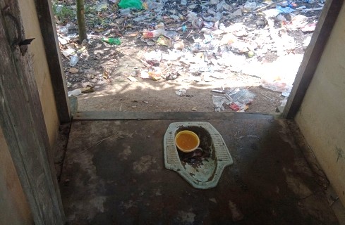 Doorway to a dirty, litter-filled outdoor area; an orange bowl rests on a feeding tray on the threshold.