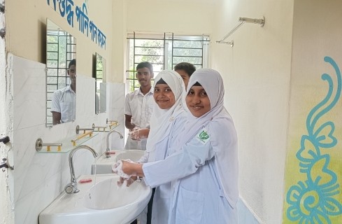Two girls in white lab coats and hijabs washing hands at sinks in a school laboratory.
