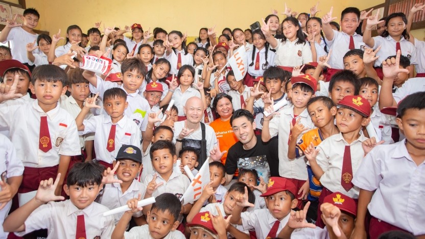 Large group of uniformed schoolchildren and a few adults posing together, many making hand signs and smiling for a group photo.
