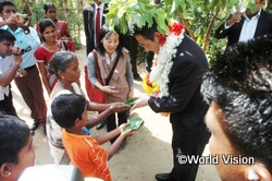 訪問先の家族から歓迎の印である緑の葉を受け取る岡田副総理