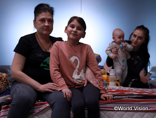 ルーマニアにあるウクライナ難民のための一時避難施設のベッドにお母さん、姉、幼い従弟とともに座るダイアナちゃん